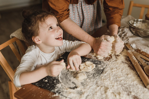 little girl kneading dough with mom