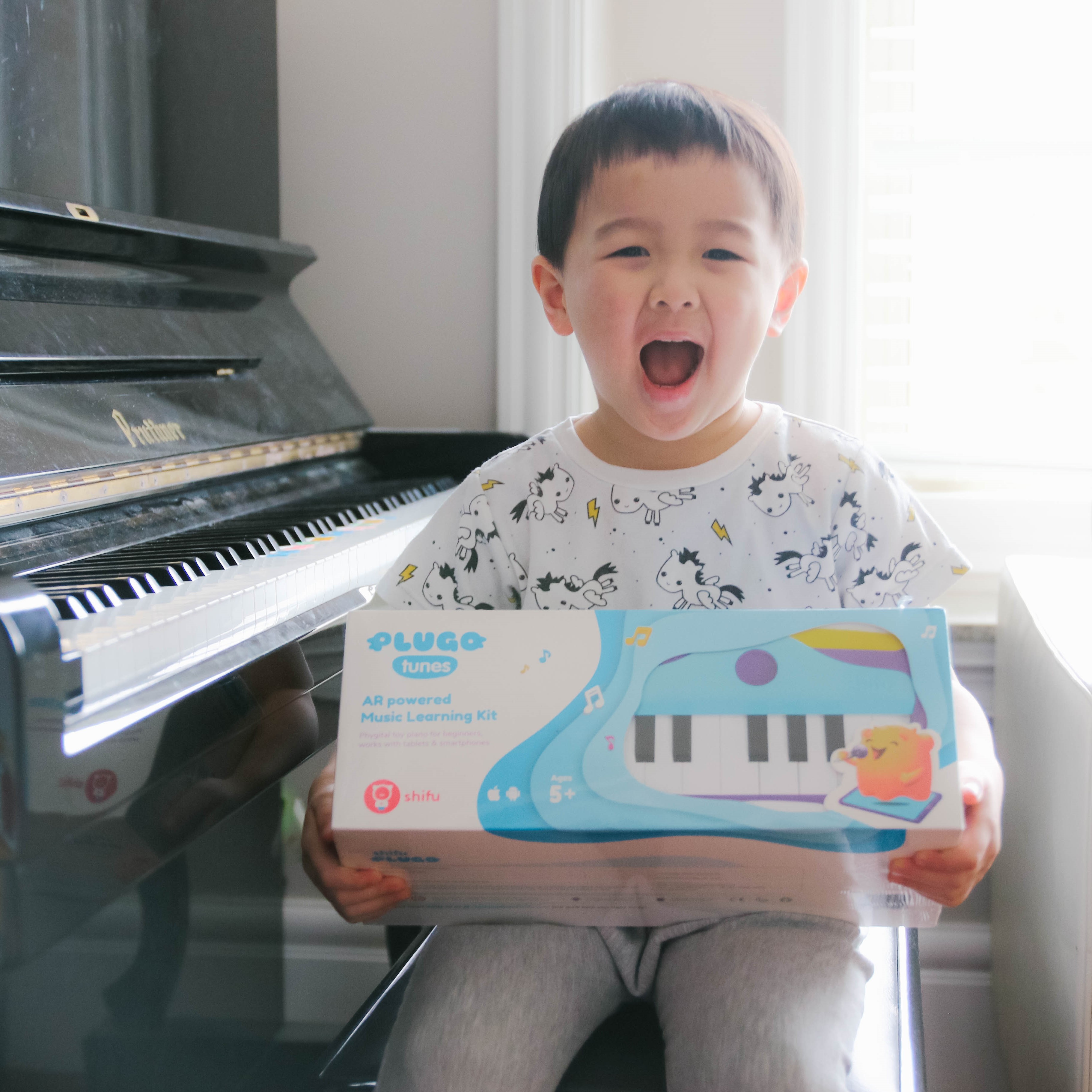 kid sitting besides a piano with Plugo tunes box