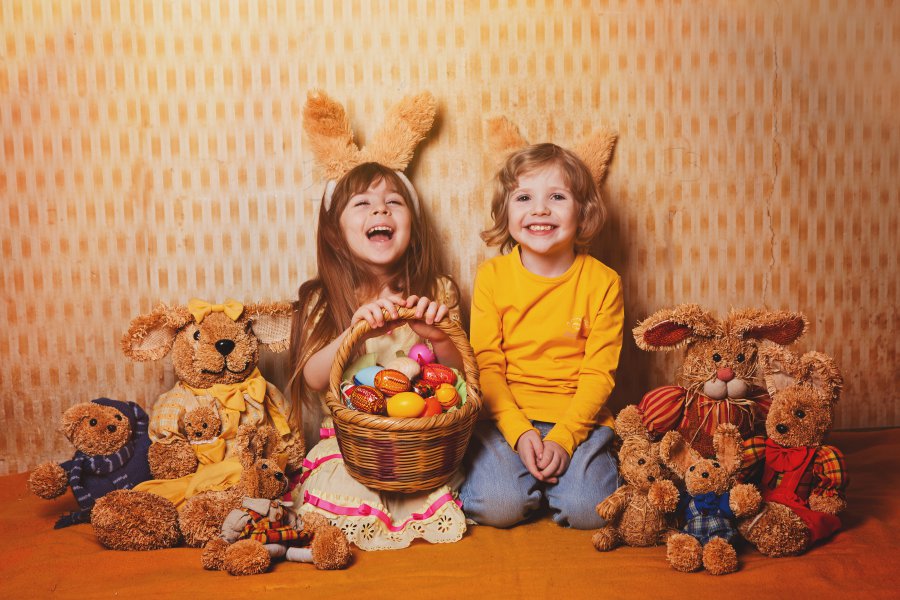 boy and girl with rabbit ears sitting around a lot of straw and plush hares, vintage style